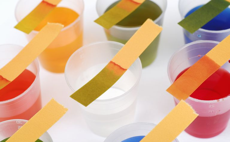 Tiras de prueba de tornasol encima de vasos de plástico con varios líquidos multicolores