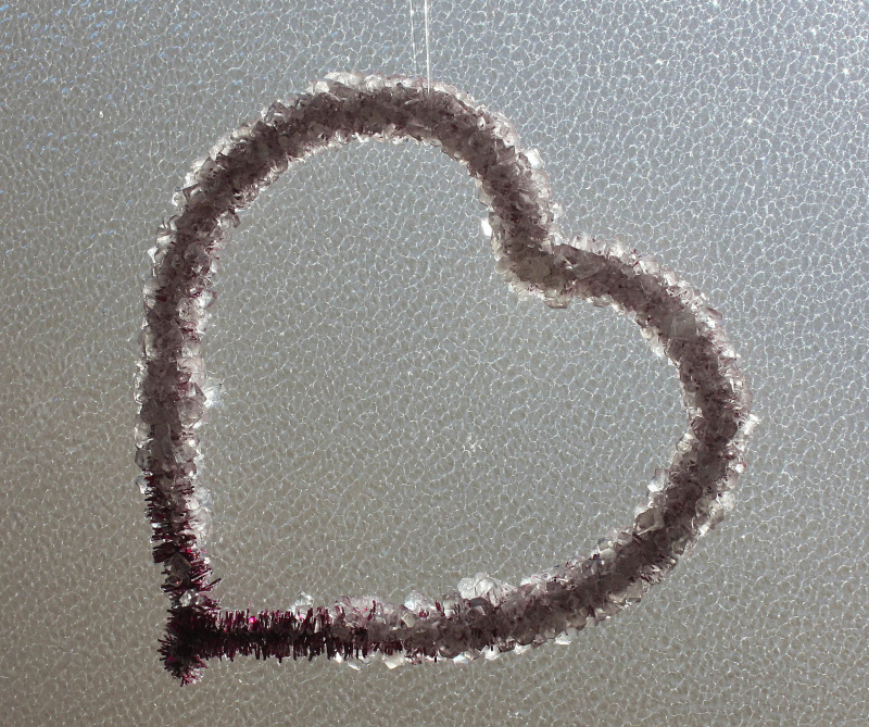 Borax-Kristalle, die über einem Chenille-Herz wachsen