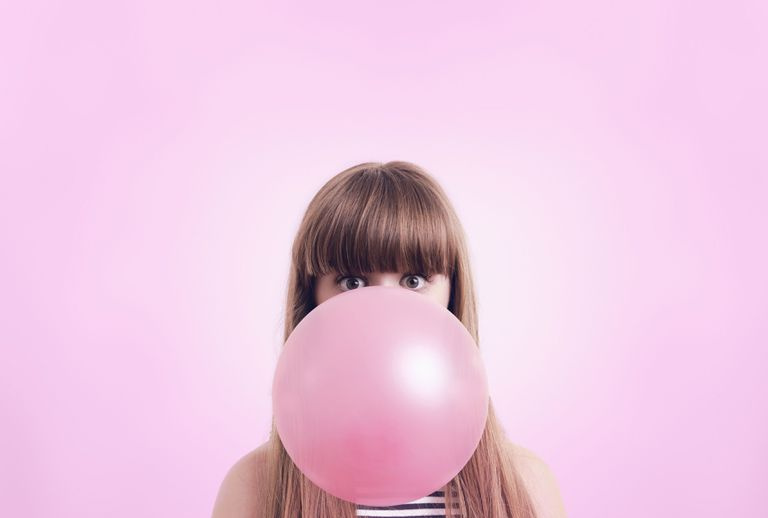 Donna che soffia grande bolla di gomma da masticare prima di sfondo rosa