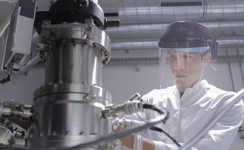 Zinātnieks stāv analītiskajā laboratorijā ar skenējošo elektronu mikroskopu un spektrometru.