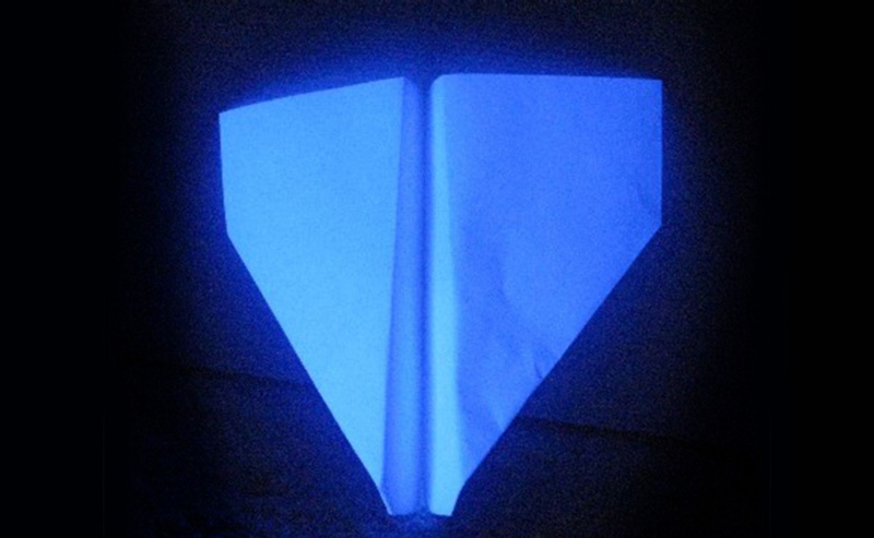 Avião de papel encostado na parede sob luz negra.