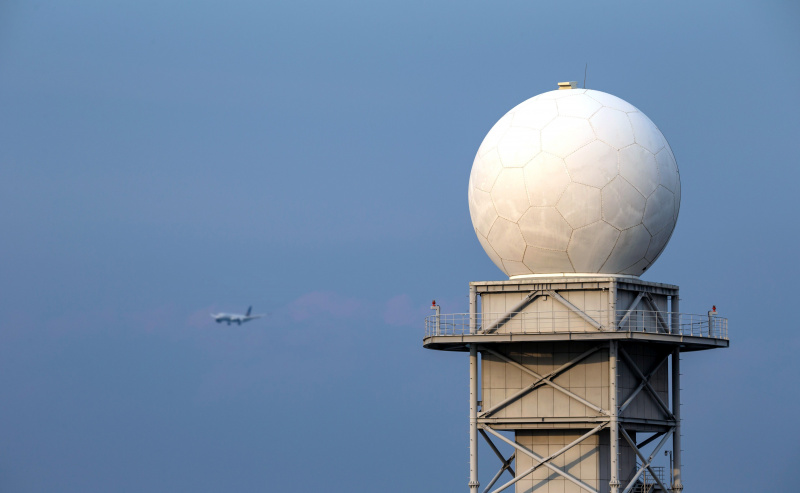 Um radar meteorológico com um céu azul e um avião ao fundo