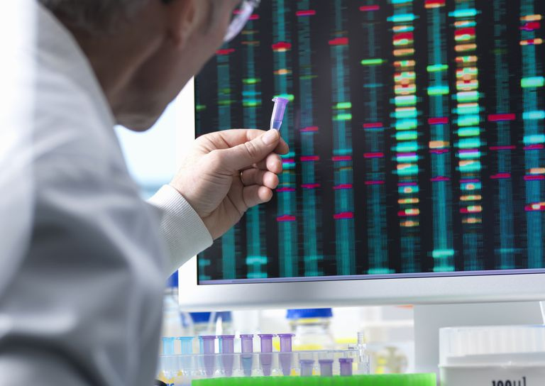 Naukowiec trzymający próbkę DNA z wynikami na ekranie komputera