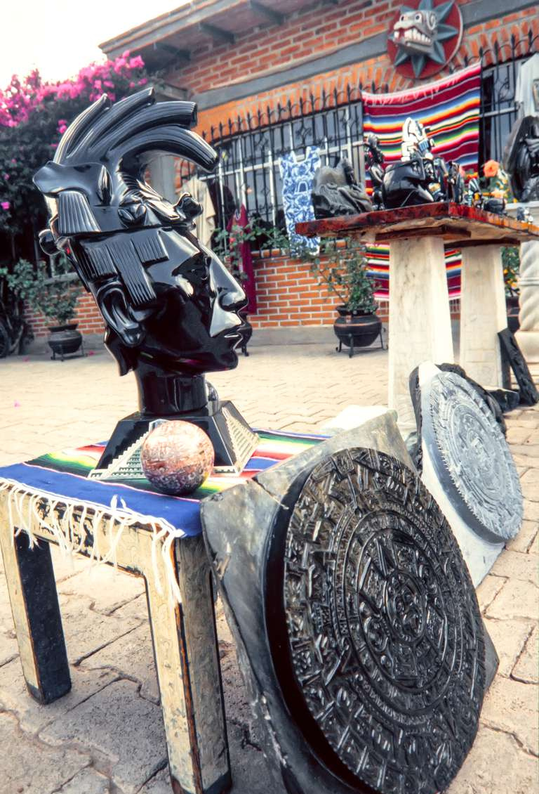 Estatua de cabeza azteca de obsidiana hecha a mano a la venta entre otros artefactos mesoamericanos.