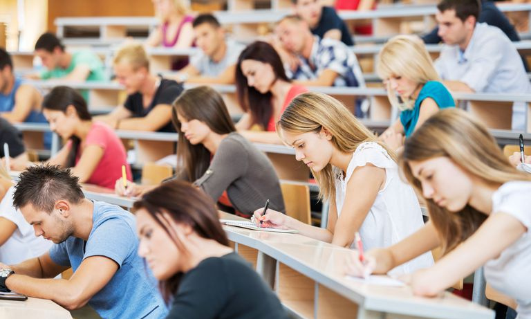 Os alunos estão sentados em filas em uma grande sala de aula.