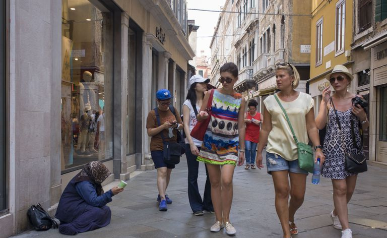 Bettelnde Person, während Touristen vorbeigehen.
