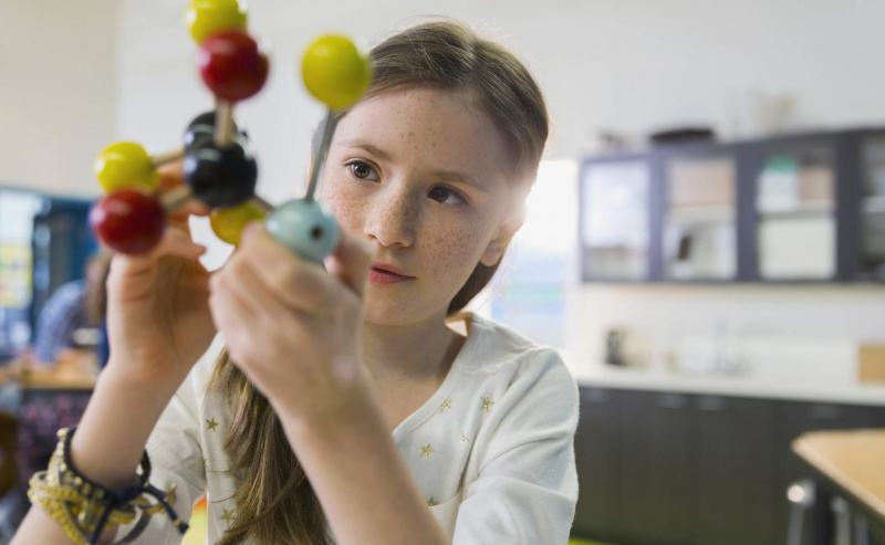 Dziewczyna studiuje molekuły w klasie chemii, ilustrując tradycyjną strukturę szans edukacji jako drogę do sukcesu w USA.