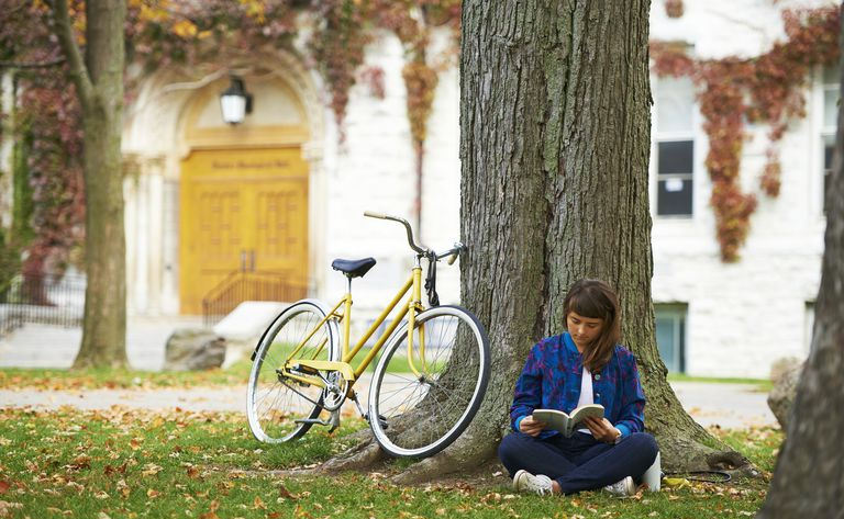 黄色の自転車で秋に大学のキャンパスで本を読んでいる女の子