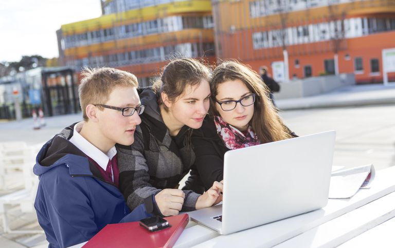 Trzech uczniów korzysta z laptopa na zewnątrz