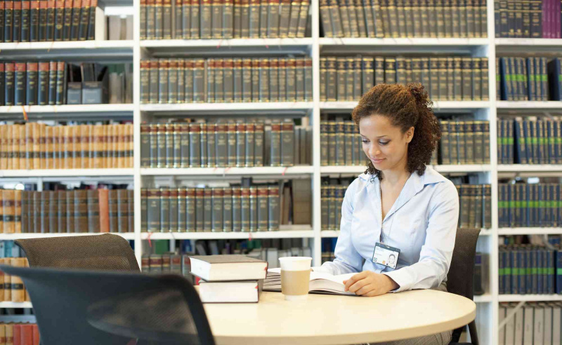 Forretningskvinne av blandet rase som leser ved skrivebordet i lovbiblioteket