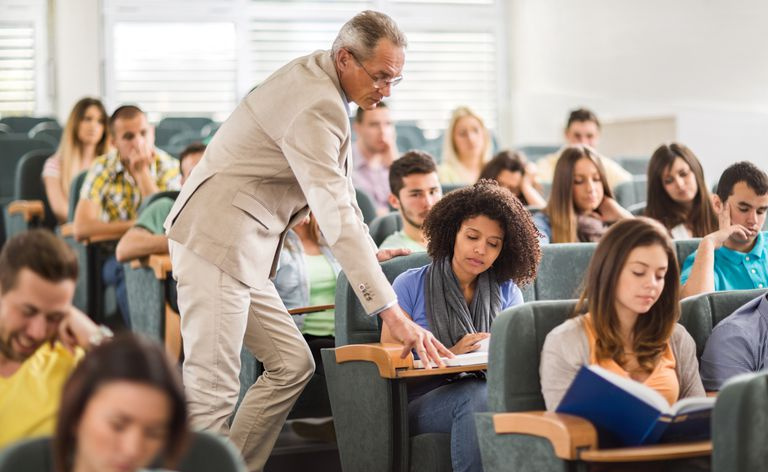 Profesor que ayuda a un estudiante afroamericano durante una conferencia en el anfiteatro.