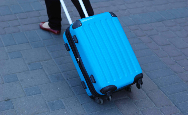 Se lleva una mochila con ruedas azul por el camino.