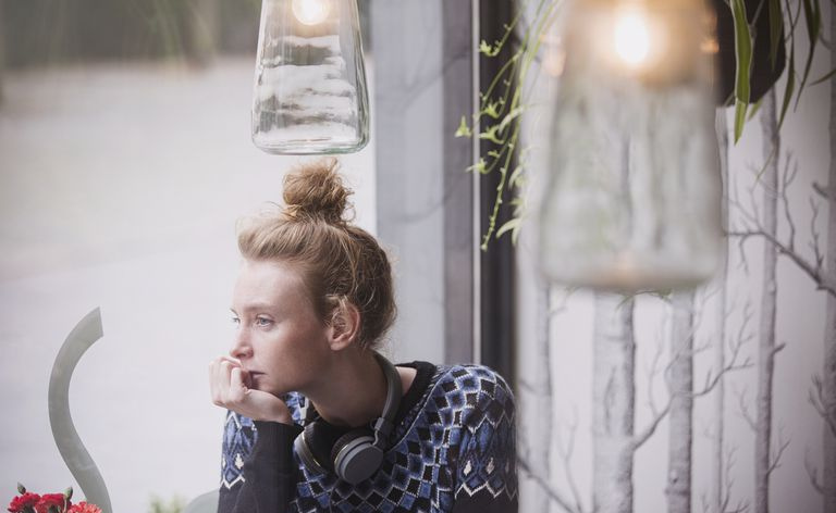 Mujer joven pensativa con auriculares en la computadora portátil mirando por la ventana del café