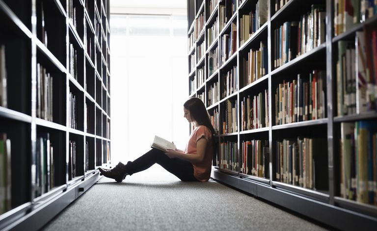 Une fille lit un livre entre deux étagères.