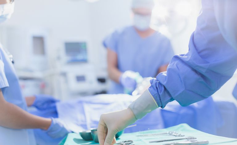Chirurg in Gummihandschuhen, der im Operationssaal nach einer chirurgischen Schere auf einem Tablett greift