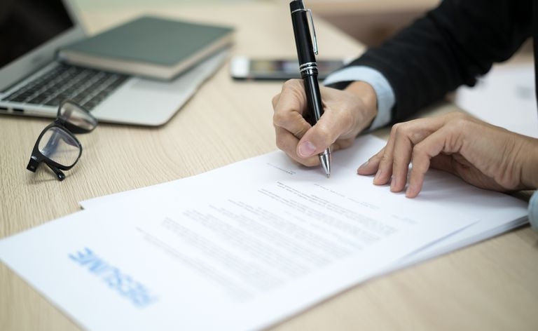 Przycięte zdjęcie kobiety podpisującej się na papierkowej robocie podania o pracę przy biurku
