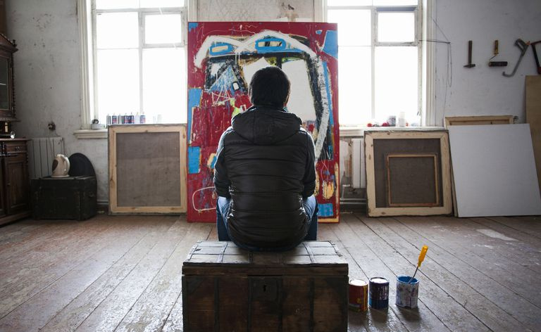 Mannlig kunstner sitter på kasse, ser på kunstverk, sett bakfra