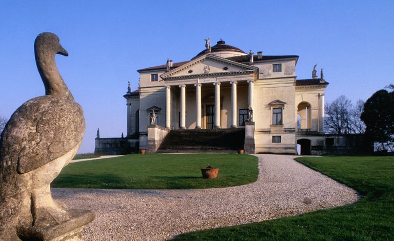 Villa diseñada por Palladio con frontón, columnas y cúpula en un entorno campestre con una escultura de un pájaro en primer plano