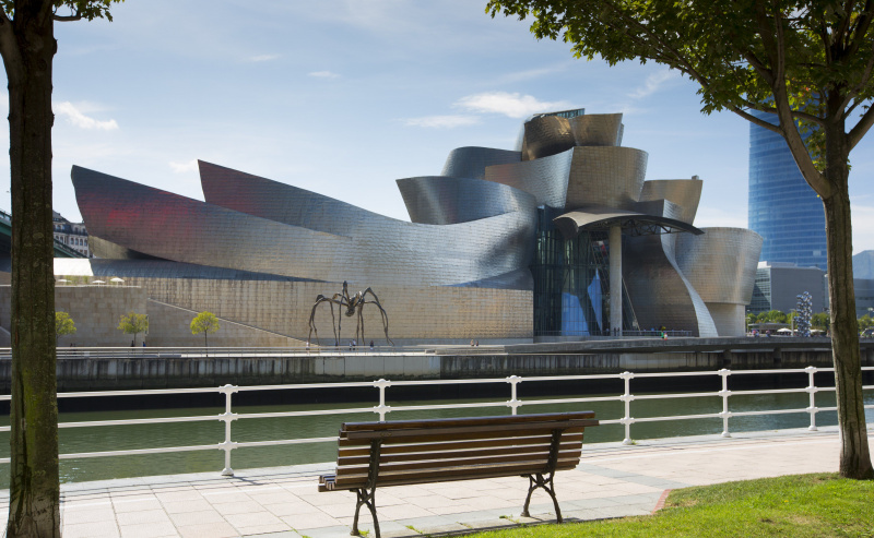 edifício de metal moderno, brilhante e curvilíneo, visto de um banco de parque em um corpo de água