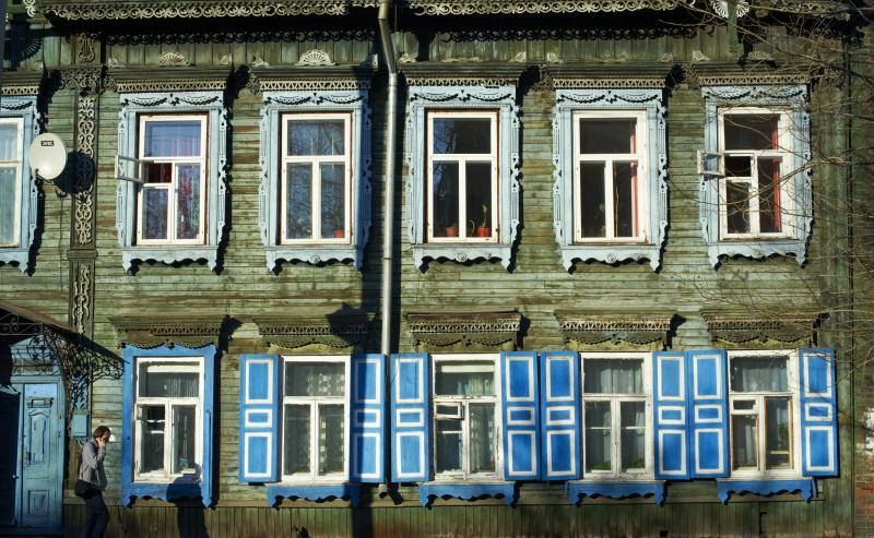 Casa de madera de dos pisos con ventanas de madera ornamentadas y persianas azules coloridas