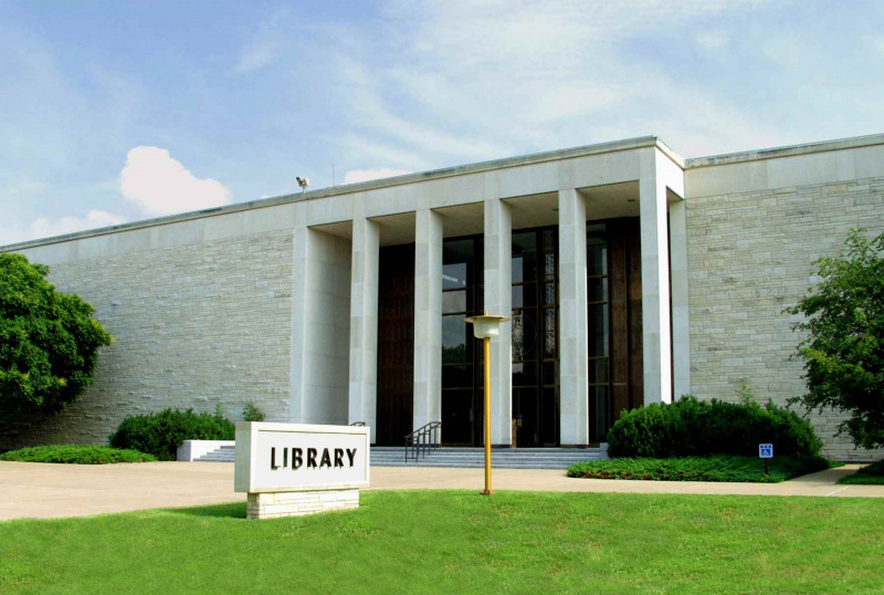 placa diz Biblioteca no gramado em frente ao prédio de pedra com cinco pilares quadrados
