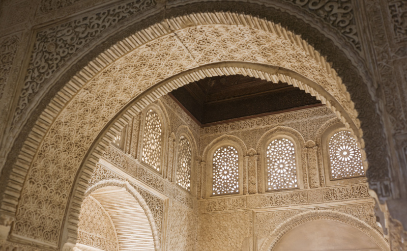 olhando através de um arco interior esculpido com ornamentos para uma sala com outros arcos e janelas em arco com treliça sobre eles