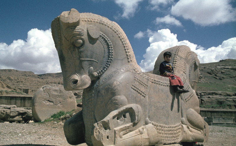 Un niño se sienta en medio de una gran estructura de piedra, entre dos cabezas de caballo.