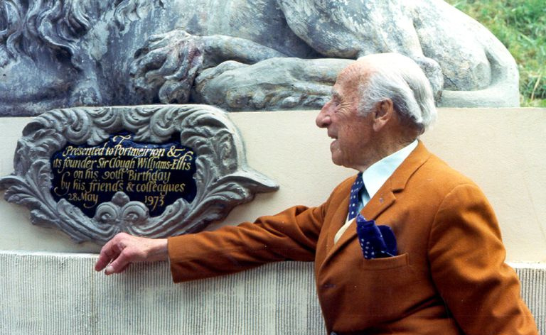 Siwowłosy Sir Clough Williams-Ellis, 90 lat, w pomarańczowo-brązowym garniturze, patrzący na tabliczkę z ozdobną żeliwną ramą w 1973 roku