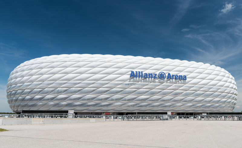 sānskats uz izliektu sporta stadionu, piepūstu ETFE plastmasas paneļu veidota ārpuse, kas izskatās kā balta protektora riepa sānos